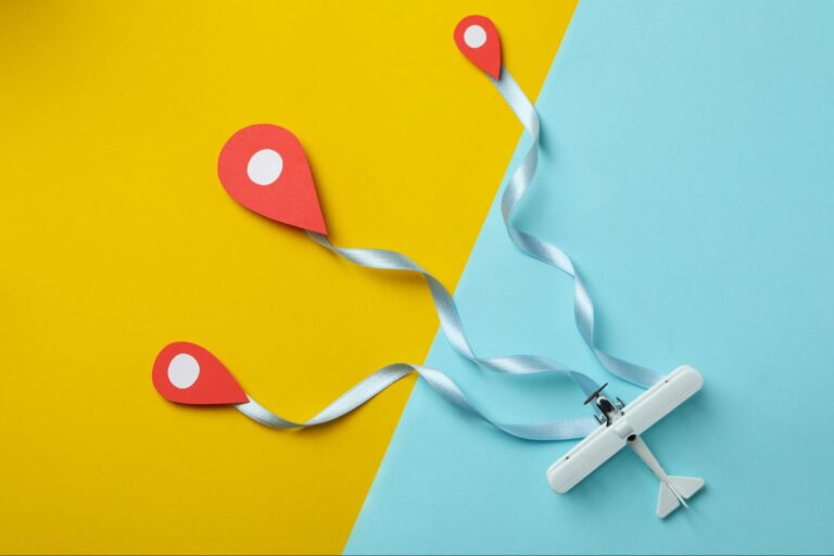 A small white toy airplane with a blue ribbon trails behind it, leading to three red location markers. The background is divided diagonally into yellow on the left side and light blue on the right side.