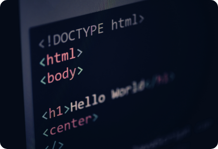 Close-up of a computer screen displaying HTML code. The code shows basic tags including `html`, `body`, and `h1`. The text "Hello World" is visible, enclosed within `h1` tags. Coding syntax is highlighted in different colors.